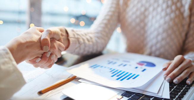 Shaking hands over laptop and financial documents; bank loan concept